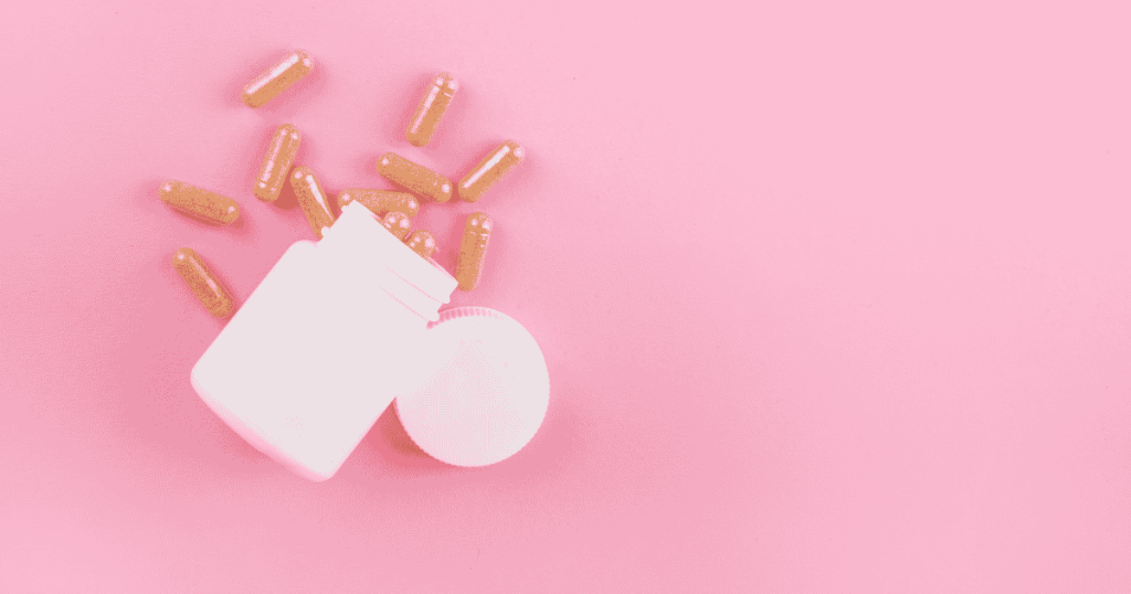 An open white supplement bottle spills light brown capsules onto a solid pink background.