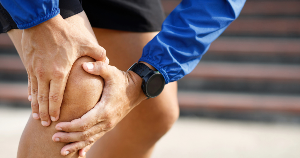 Close-up of an athlete in a blue jacket holding their painful knee.