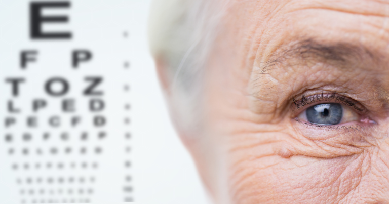 A close-up of an elderly person's blue eye on the right side of the image, with a blurred Snellen eye test chart visible in the background on the left.